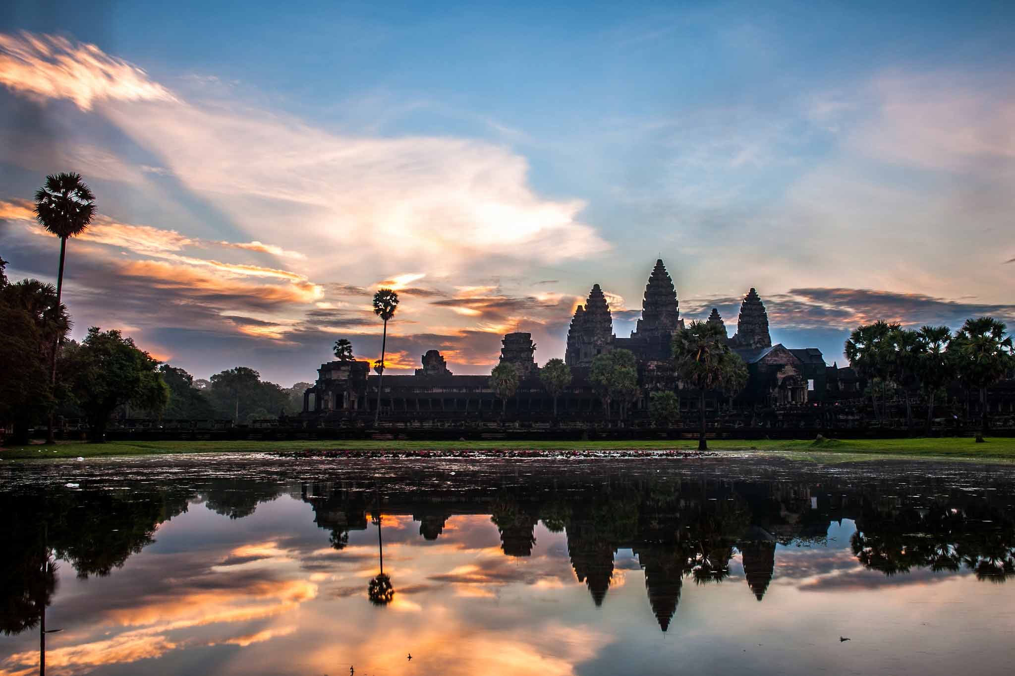 Silhouette of Angkor Wat temple against a pink and purple sky during sunrise.