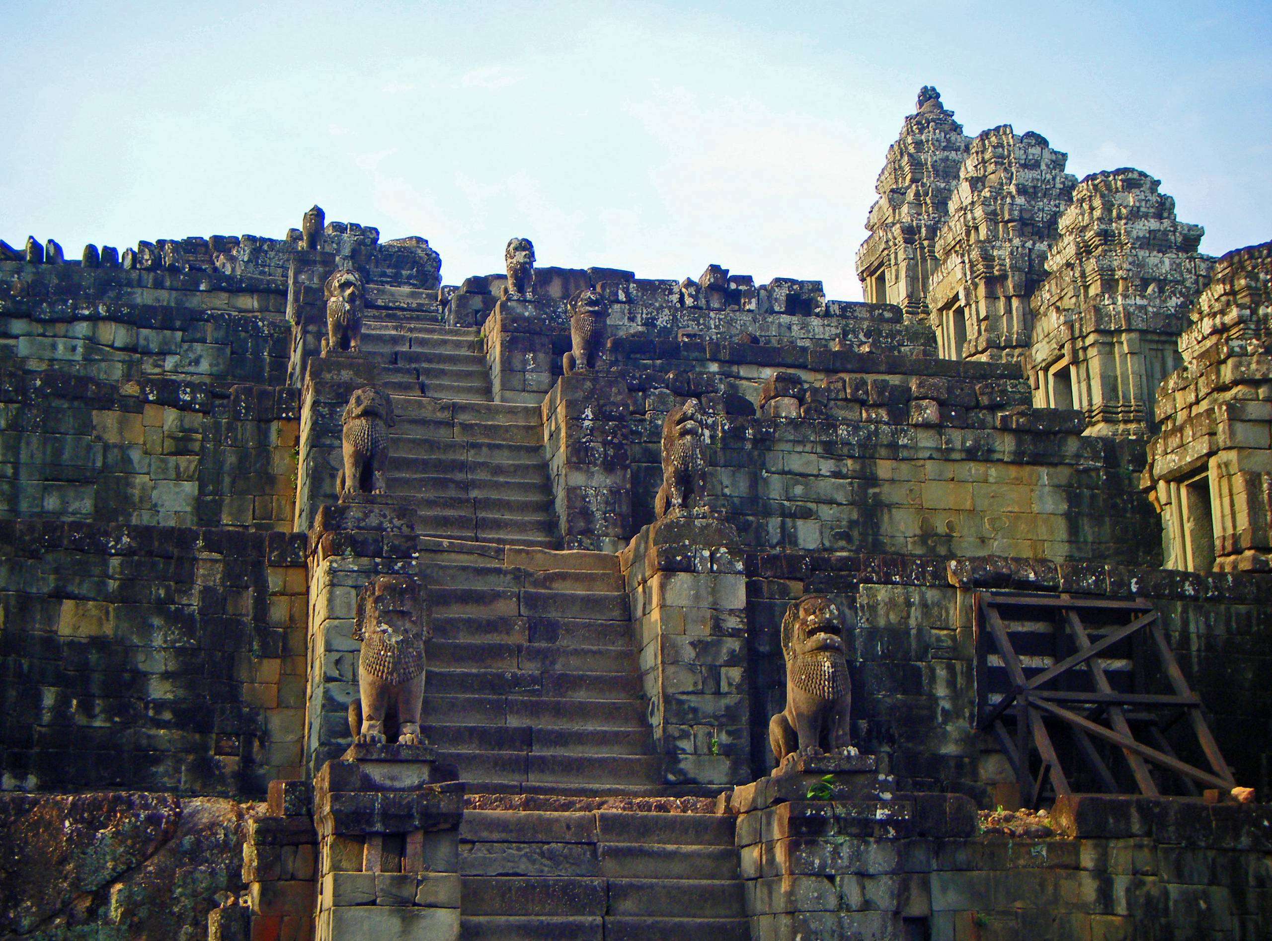 A stone staircase leading up to the entrance of Phnom Bakheng, with trees and jungle surrounding it